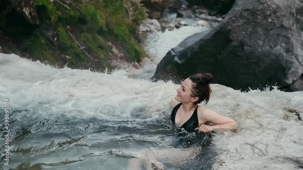 Natural hot springs pool - a woman relaxes in a geothermal spa in the Kuril Islands. The girl enjoys swimming in the lagoon with blue water among the green forest. Kuril tourist attraction. Natural hot springs pool - a woman relaxes in a geothermal spa in the Kuril Islands. The girl enjoys swimming in the lagoon with blue water among the green forest. Kuril tourist attraction.