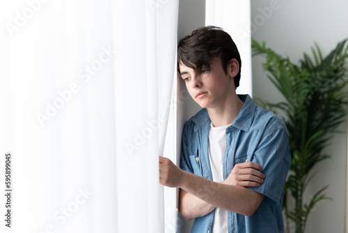 Sad teenager boy looking through window photo