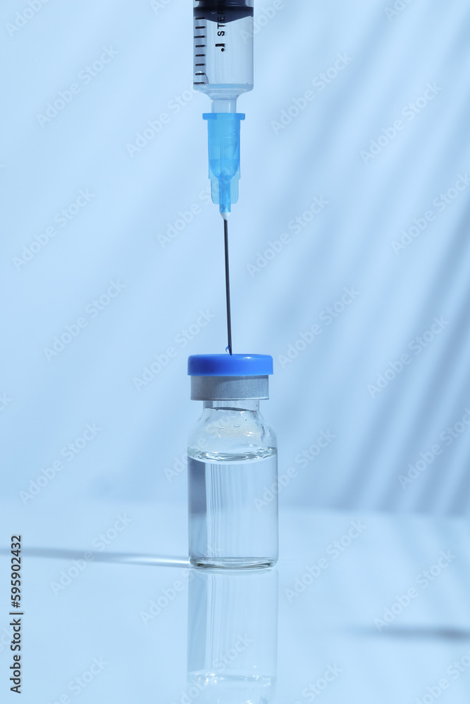Syringe inserted into a vaccine bottle to draw liquid medicine, cool toned image, blue color temperature Syringe inserted into a vaccine bottle to draw liquid medicine, cool toned image, blue color temperature