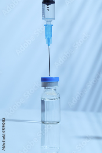 Syringe inserted into a vaccine bottle to draw liquid medicine, cool toned image, blue color temperature