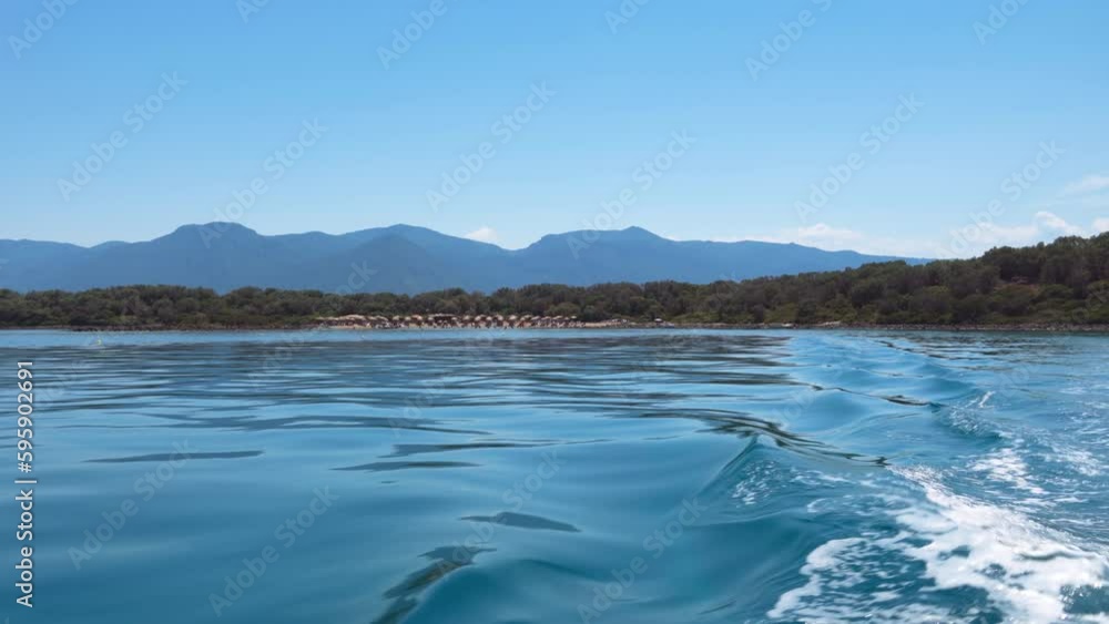 Sailing away ship day POV view looking to a rocky coastline with green vegetation and a beach with unidentifiable bathers. Sailing away ship day POV view looking to a rocky coastline with green vegetation and a beach with unidentifiable bathers.