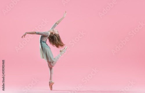 elegant young ballerina in pointe shoes dancing on a delicate pink background photo