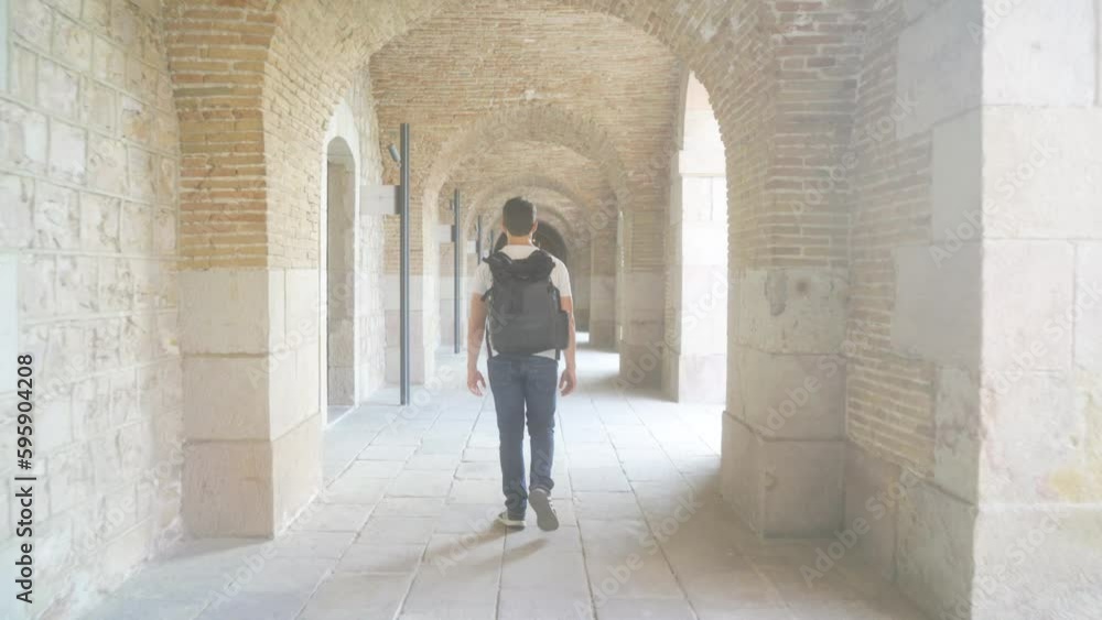 Young man with backpack walking through Montjuic castle hallway, visiting museum on sunny day on holiday and sightseeing historical military fortress; relaxed vacation stroll Young man with backpack walking through Montjuic castle hallway, visiting museum on sunny day on holiday and sightseeing historical military fortress; relaxed vacation stroll