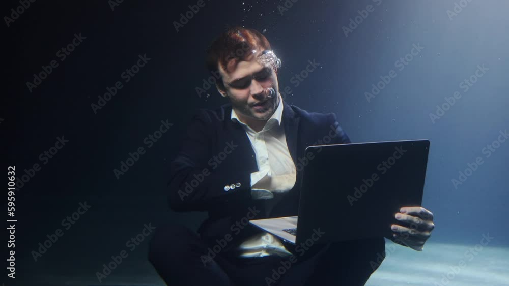 A businessman in a suit is working on a laptop underwater. A businessman in a suit is working on a laptop underwater.