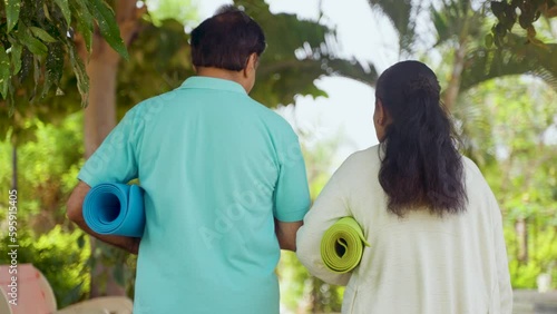 rear view trackig shot of Indian senior couple with yoga mat at park for exercising - concept of healthy active lifestyle, relaxation and relationship bonding. photo