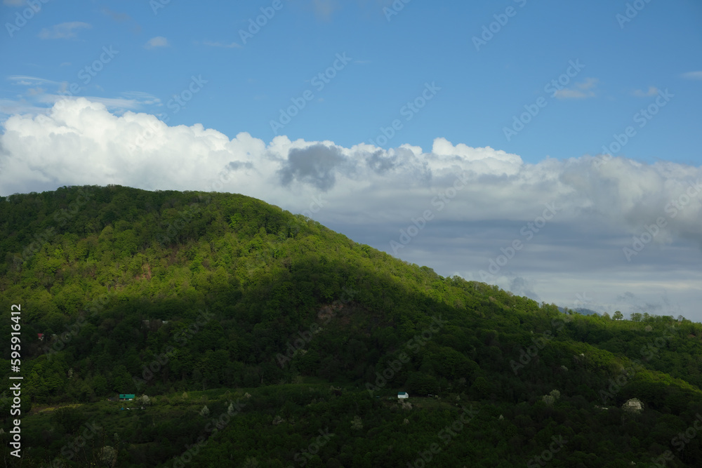 General plan of green hills illuminated by sun rays breaking through the clouds against the blue sky in the summer season