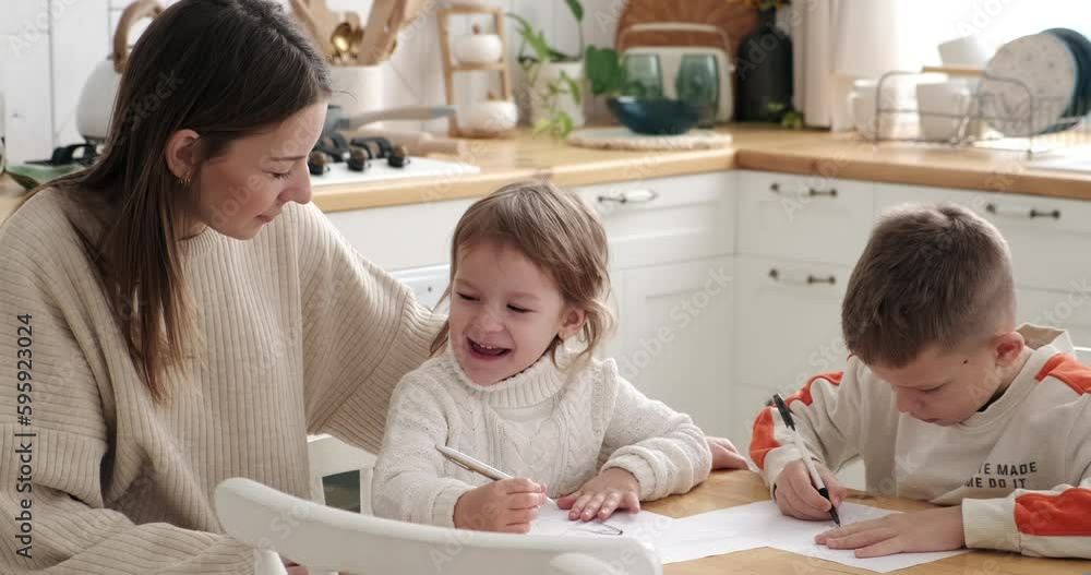 Mother spending leisure time and helping her children drawing a sketch on paper at home Mother spending leisure time and helping her children drawing a sketch on paper at home