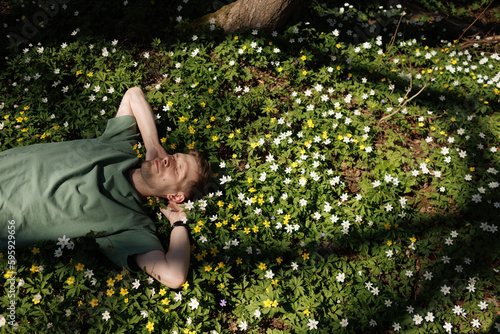 Young man laying in green grass with flowers. People fatigue from work. Summer sleeping and relaxation techniques. Vitamin D sunbathing. Man power nap with eye closed. Rest after work from home