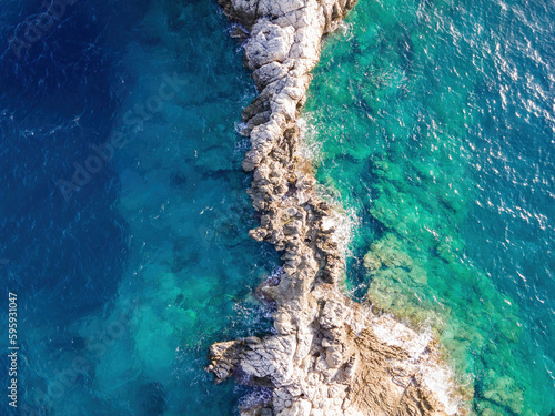 Top aerial view of azure sea waves crashing at rocky cliff