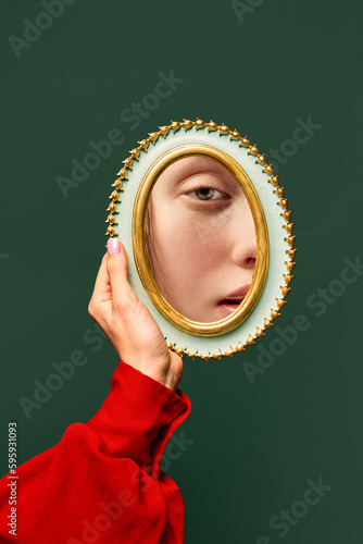 Fotografia Female hand holding small mirror with reflection of sad woman's face with natural make up over dark green background