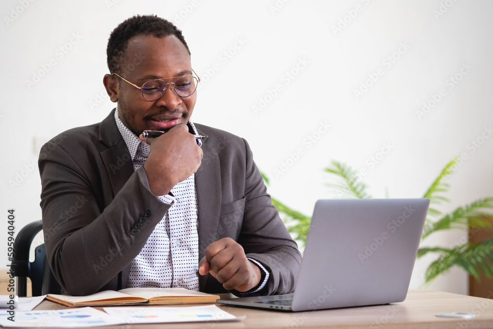 African American businessman analyzing laptop graph paperwork in office holding documents preparing portfolio analysis report Black male analyst doing paperwork in the workplace using the computer. African American businessman analyzing laptop graph paperwork in office holding documents preparing portfolio analysis report Black male analyst doing paperwork in the workplace using the computer.