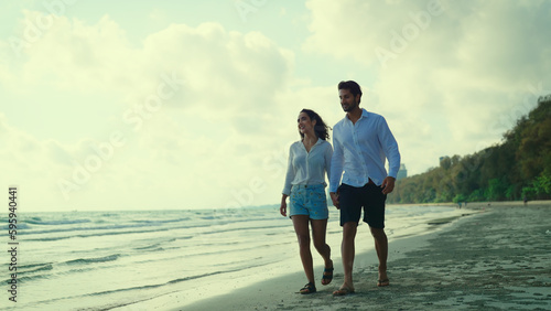 Obraz na plátně Young couple takes a leisurely stroll along the beach, their smiles beaming as they chat and laugh together, enjoying each other's company in the peaceful setting