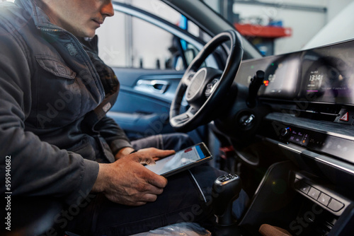 Cropped picture of a mechanic sitting in a car with tablet in his hands and doing technical review and diagnostics at mechanic's shop. © dusanpetkovic1