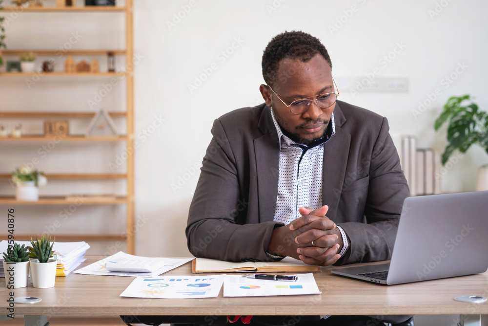 African American businessman analyzing laptop graph paperwork in office holding documents preparing portfolio analysis report Black male analyst doing paperwork in the workplace using the computer. African American businessman analyzing laptop graph paperwork in office holding documents preparing portfolio analysis report Black male analyst doing paperwork in the workplace using the computer.