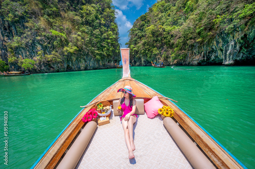 Asian woman in pink bikini sitting on a boat floating in Koh Hong Lagoon with blue-green water and mountains in the background.Thailand photo