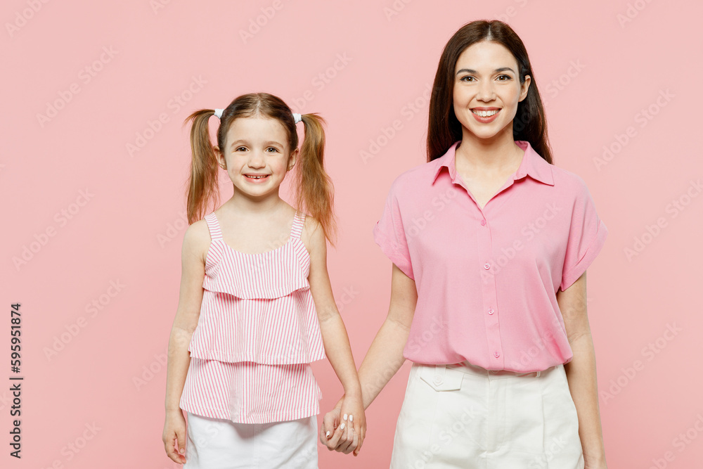 Happy smiling cheerful fun woman wearing casual clothes with child kid girl 6-7 years old. Mother daughter hold hands look camera isolated on plain pastel pink background. Family parent day concept. Happy smiling cheerful fun woman wearing casual clothes with child kid girl 6-7 years old. Mother daughter hold hands look camera isolated on plain pastel pink background. Family parent day concept.