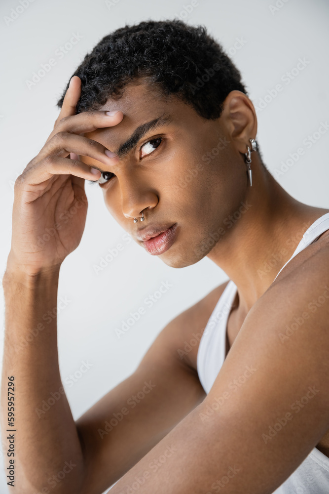 portrait of african american man with silver piercing holding hand near forehead and looking at camera isolated on grey. portrait of african american man with silver piercing holding hand near forehead and looking at camera isolated on grey.