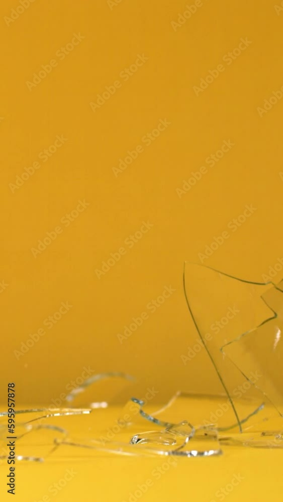 Glass tumbler falls and shatters into pieces on a solid bright background in slow motion Glass tumbler falls and shatters into pieces on a solid bright background in slow motion