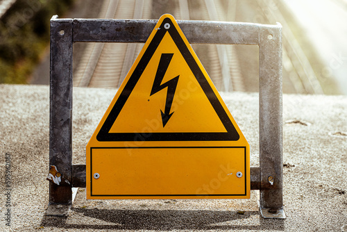 warn-Schild strom auf einer brück an einem bahngleis bei sonnenschein photo