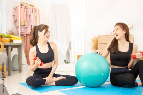 Two beautiful Asian girls wearing workout clothes and smiling with dogs in bedroom. woman on exercise mat with dumbbells and tablet.