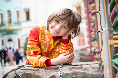  a happy boy in a Russian national bright red-orange costume near the Russian national multi-colored Terem building. photo