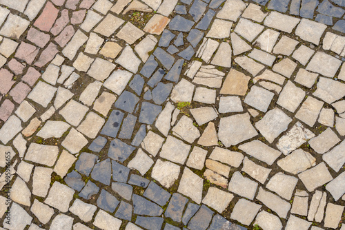 A road paved with stones, a green grass between stones on the sidewalk.