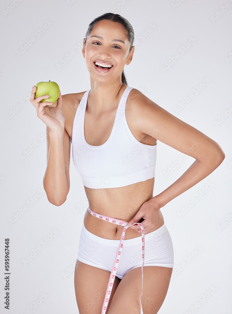 Eat healthy and watch those inches disappear. Studio portrait of an attractive young woman eating an apple and using a measuring tape against a grey background. Eat healthy and watch those inches disappear. Studio portrait of an attractive young woman eating an apple and using a measuring tape against a grey background.