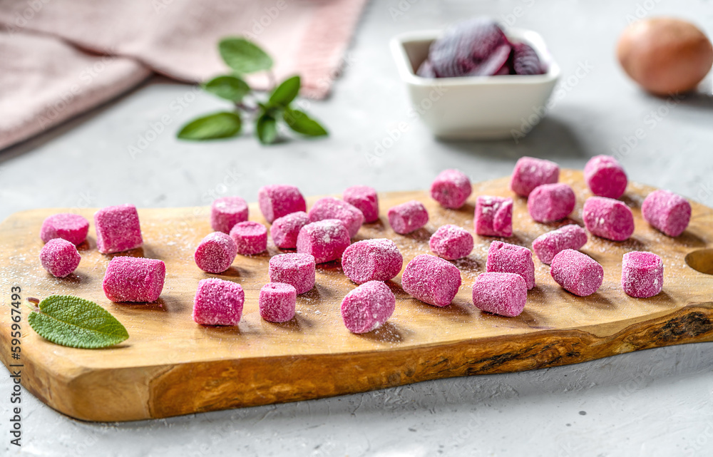 Beetroot and potato homemade gnocchi on wooden cutting board, ingredients, sage leaves, napkin, grey concrete background Beetroot and potato homemade gnocchi on wooden cutting board, ingredients, sage leaves, napkin, grey concrete background