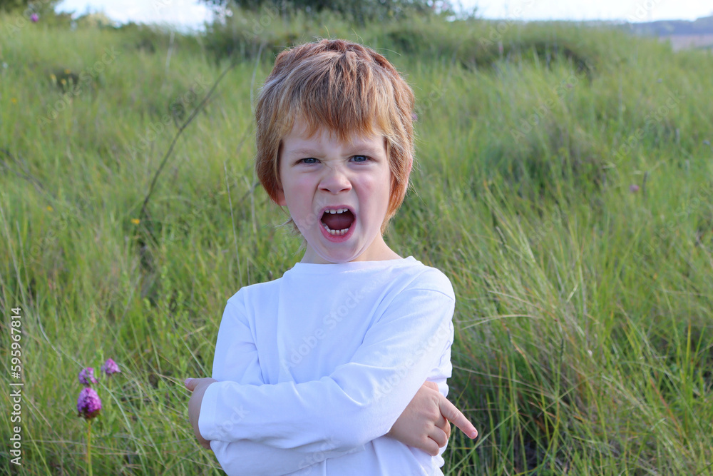 The blond boy furrowed his nose and opened his mouth wide. five year old boy in a bad mood. The blond boy furrowed his nose and opened his mouth wide. five year old boy in a bad mood.