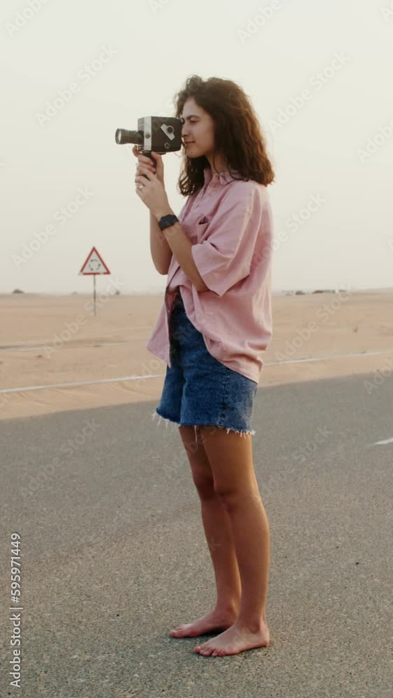 A young woman of European appearance shoots a video standing barefoot on a road covered with sand in the desert A young woman of European appearance shoots a video standing barefoot on a road covered with sand in the desert