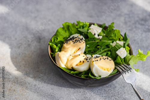 Bowl of mixed salad leaves with boiled eggs, feta cheese, mayonnaise and sesame seeds photo