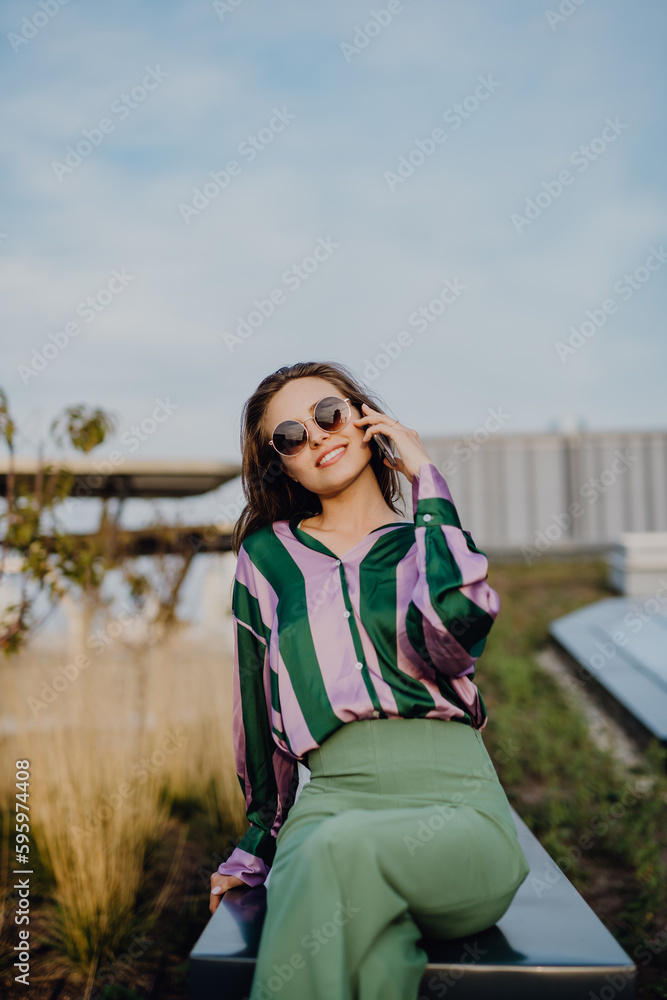 Portrait of beautiful young woman with smartphone outdoor in city, during sunset.