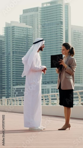 A business woman of European appearance shows her Arab partner documents while standing on the street of a modern metropolis photo