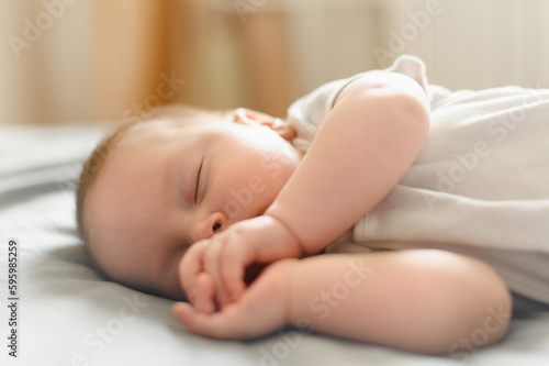 Cute baby sleeps peacefully in his crib at home, lying on his side. The concept of independent sleep, childhood protection.