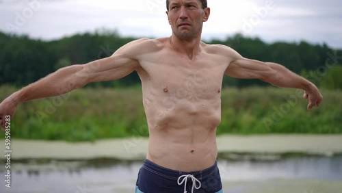 Medium shot shirtless sportsman exercising outdoors warming up before training. Portrait of serious motivated Caucasian adult man working out in spring summer park. Slow motion photo