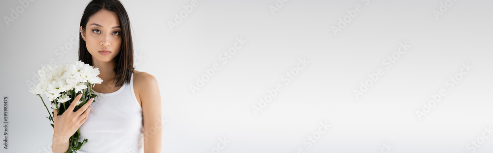 young asian woman with bouquet of white flowers looking at camera isolated on grey, banner. young asian woman with bouquet of white flowers looking at camera isolated on grey, banner.