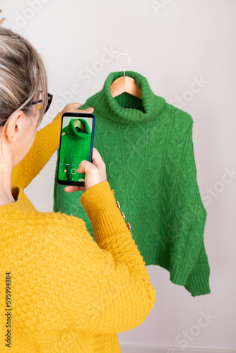 woman with phone in hand, taking photos of used clothes to sell in second-hand app, vertical
