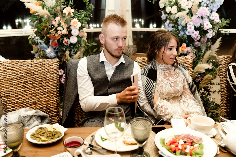 a young groom with a beard and a satisfied bride are sitting at the wedding table at a banquet. wedding couple at the banquet. festive food on the wedding day a young groom with a beard and a satisfied bride are sitting at the wedding table at a banquet. wedding couple at the banquet. festive food on the wedding day