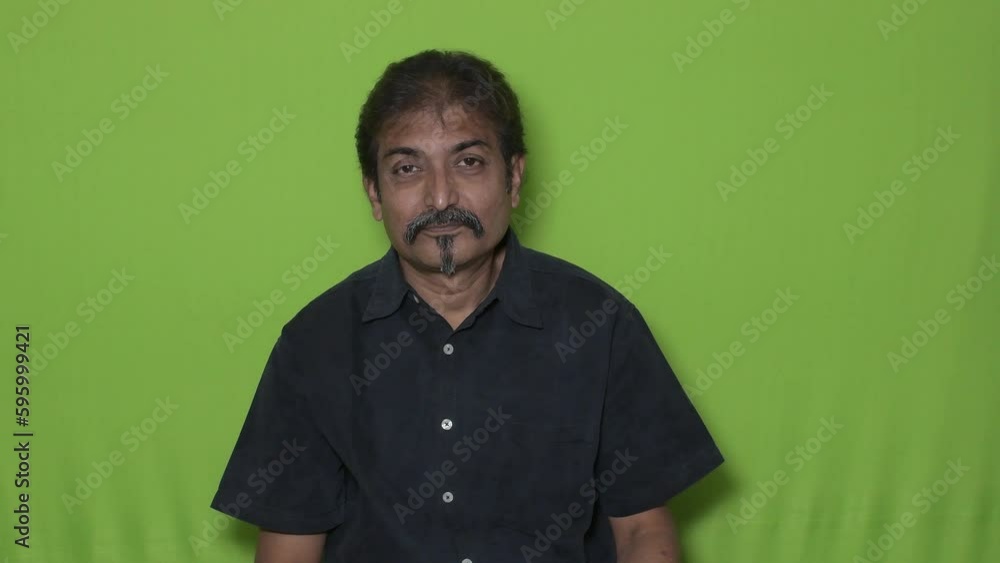 The well-dressed Indian man wearing a black shirt is indicating something to his right up direction with his left hand's index fingers while standing against a green screen background The well-dressed Indian man wearing a black shirt is indicating something to his right up direction with his left hand's index fingers while standing against a green screen background