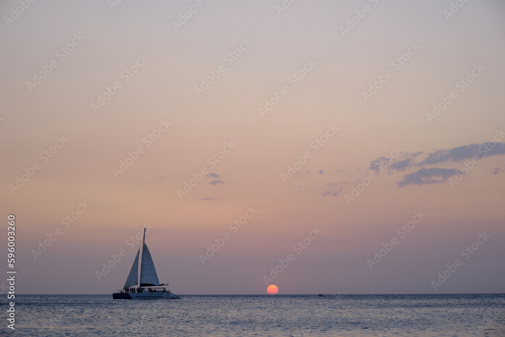 A sailboat on a sunset cruise off the coast of Aruba. The sun is at the horizon and light is fading. 