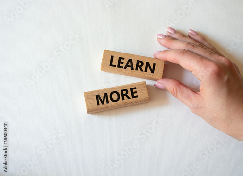 Learn more symbol. Concept word Learn more on wooden blocks. Beautiful white background. Businessman hand. Business and Learn more concept. Copy space