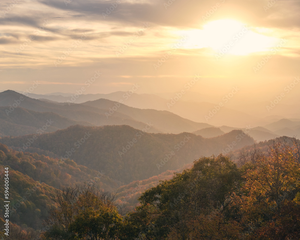 Obraz premium A beautiful sunset over the smoky mountains in North Carolina. It is a hazy day with a lot of clouds in the sky, but the sun is shining through for a beautiful image.