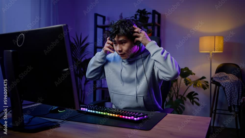 Young Asian guy, professional gamer puts on headphones and starts playing stream online video games Young Asian guy, professional gamer puts on headphones and starts playing stream online video games