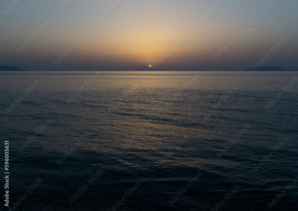 stunning blue and yellow sunset over mediterranean ocean with rounded orange sun and calm sea