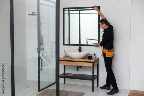 The worker installs the mirror in the bathroom.