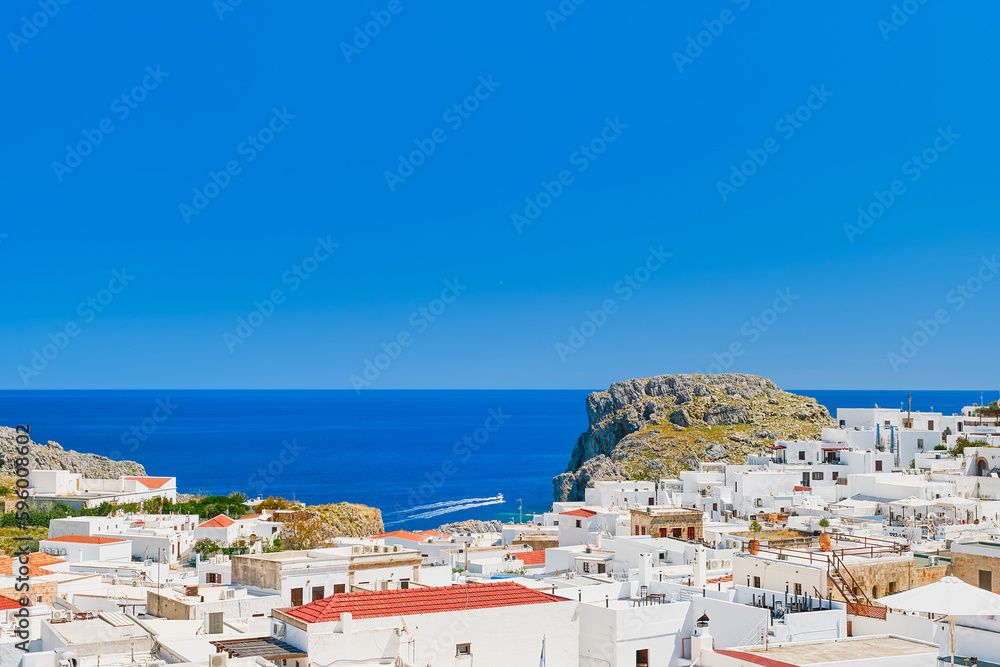 Rooftop view of the city of Lindos and the emerald sea with passing boats, Rhodes island, Greek islands of the Dodecanese archipelago, Europe. Vacation and popular travel destination