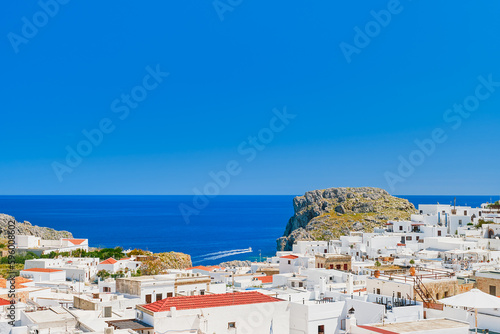 Rooftop view of the city of Lindos and the emerald sea with passing boats, Rhodes island, Greek islands of the Dodecanese archipelago, Europe. Vacation and popular travel destination