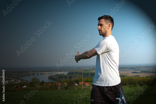 a young guy in a white shirt is stretching, behind him is a beautiful landscape, training in nature, a healthy lifestyle
