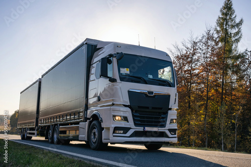 Truck is driving through the forest in autumn. Car transport . Truck with semi-trailer in gray color.