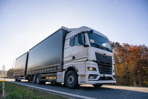 Truck is driving through the forest in autumn. Car transport . Truck with semi-trailer in gray color. © Chawran